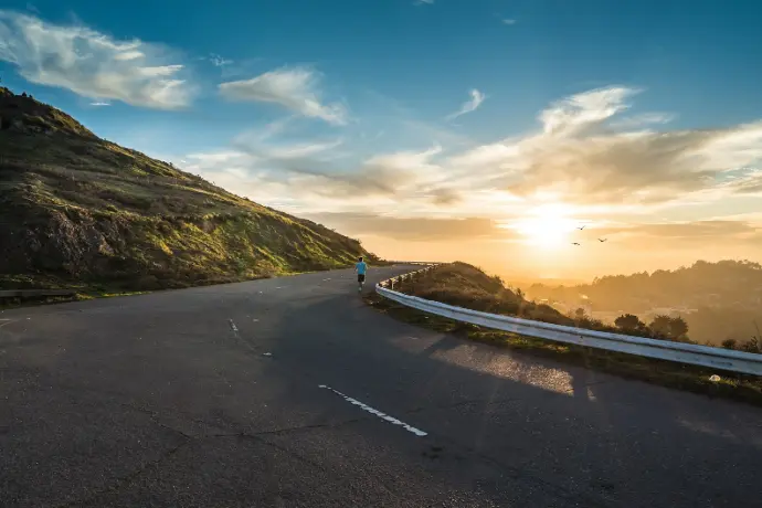 person running on road street cliff during golden hour